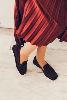 Photo of women's legs in a stylish suede burgundy loafers. Woman wearing red skirt