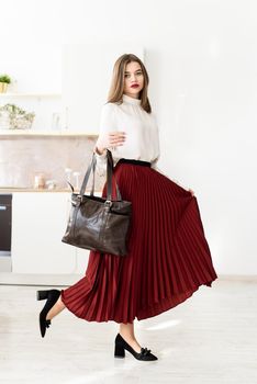 Portrait of fashionable women in a red skirt, white blouse and stylish suede shoes with a buckle posing on the kitchen. Girl with a big red lips