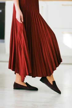 Photo of women's legs in a stylish suede burgundy loafers. Woman wearing red skirt