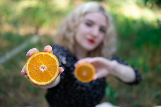 portrait of a charming blonde teenage girl with a fresh orange outdoors in forest or park. tasty juicy fruit.