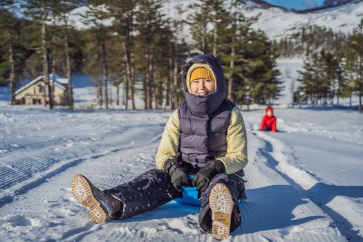 Happy woman having fun during rolling down the mountain slope on sled. Winter sports with snow. People riding a sledge.