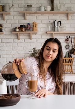 Alternative coffee brewing. young woman in lovely pajamas drinking coffee with milk at home kitchen