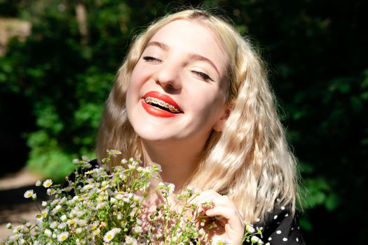 portrait of a charming blonde teenage girl wearing teeth braces with bouquet of white wildflowers. female with braces in mouth. healthy teeth. orthodontist dentist.
