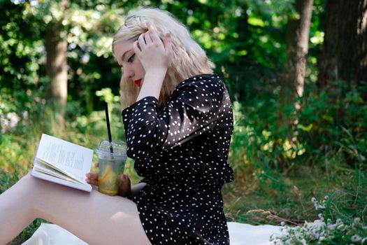 portrait of young woman on a picnic on plaid in park reading a book with tasty snacks.