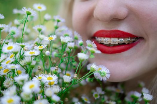 portrait of a charming blonde teenage girl wearing teeth braces with bouquet of white wildflowers. female with braces in mouth. healthy teeth. orthodontist dentist.