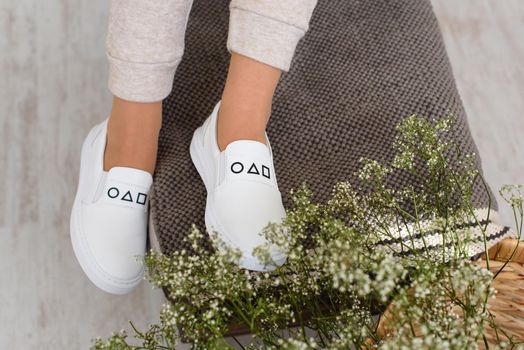 photo of a womens legs in beige sports suit and stylish white leather sneakers posing on a bench. selective focus. Indoors