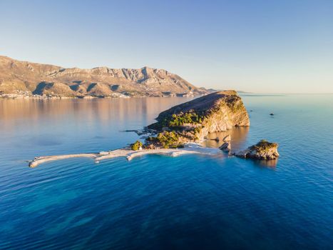 Aerial view of Sveti Nikola, Budva island, Montenegro. Hawaii beach, umbrellas and bathers and crystal clear waters. Jagged coasts with sheer cliffs overlooking the transparent sea. Wild nature.