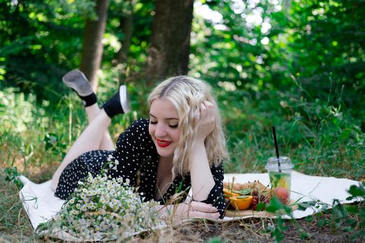 charming blonde young woman on a picnic on plaid in park with tasty snacks. Lemonade, fruits and croissants. summertime, rest, relax, enjoy. freedom.