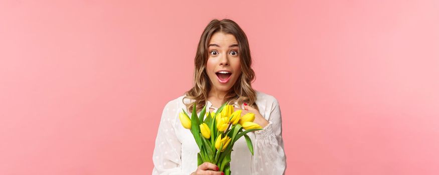Spring, happiness and celebration concept. Close-up of surprised and wondered young blond girl in white dress, receive yellow tulips and pointing herself with disbelied and amazement, didnt expact.