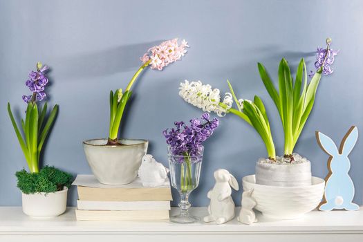 White hyacinth in a large porcelain bowl, figurines of hares and a bird, are on the fireplace against the dark blue wall. Layout. Spring concept