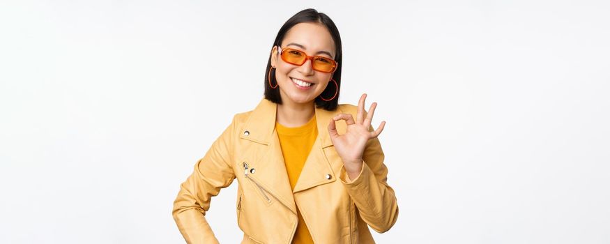 Excellent. Smiling asian girl shows okay, ok sign, nod in approval, recommending smth good, standing over white background. Copy space
