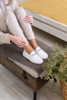 photo of a womens legs in beige sports suit and stylish white leather sneakers posing on a bench. selective focus. Indoors