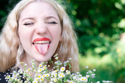 portrait of a charming blonde teenage girl wearing teeth braces with bouquet of white wildflowers. female with braces in mouth. healthy teeth. orthodontist dentist.