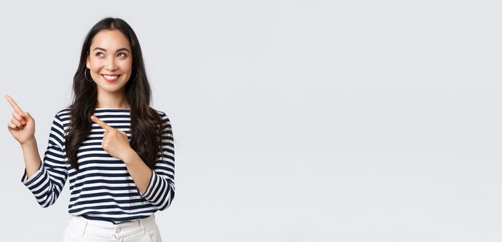 Lifestyle, people emotions concept. Excited good-looking asian girl smiling pleased as found excellent product, pointing fingers left at advertisement and looking satisfied, recommend promo.