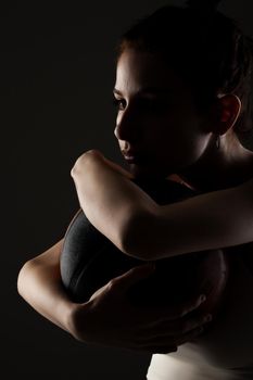 Teenage girl with basketball. Side lit studio portrait against dark background.