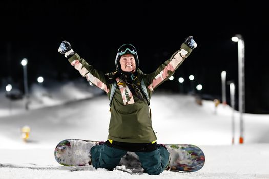 Snowboarder girl posing on slopes. Night skiing in winter resort.