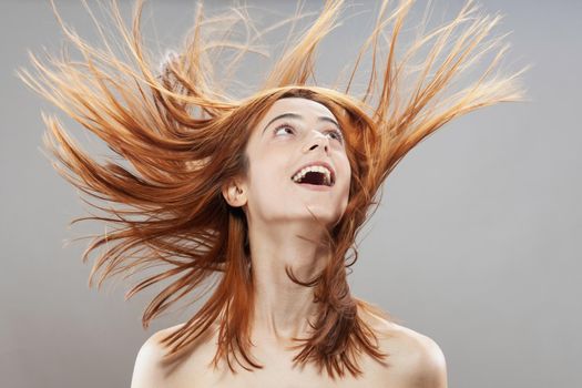 Beautiful dark burnt orange windy hair girl smiling. Studio portrait with happy face expression against gray background.