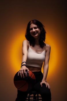 Teenage girl with dental braces holding basketball. Studio portrait on orange colored background.
