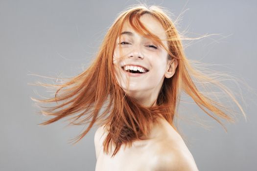 Beautiful dark burnt orange windy hair girl smiling. Studio portrait with happy face expression against gray background.