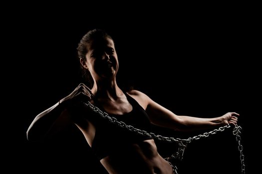 Strong fit girl with metal chain. Pulling and posing against black background