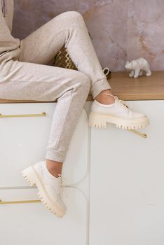 Part photo of a women in beige sports suit and stylish leather oxfords shoes posing on the kitchen. Indoors