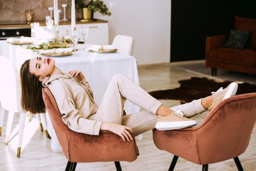 photo of a women in beige sports suit and stylish leather sneakers posing in the chair on a kitchen . selective focus. Indoors