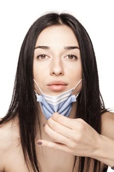 Serious looking girl pulling away medical face mask. Portrait against white background.