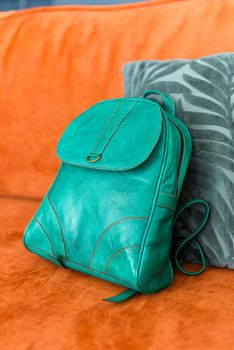 A green leather modern backpack on a orange sofa. Indoors