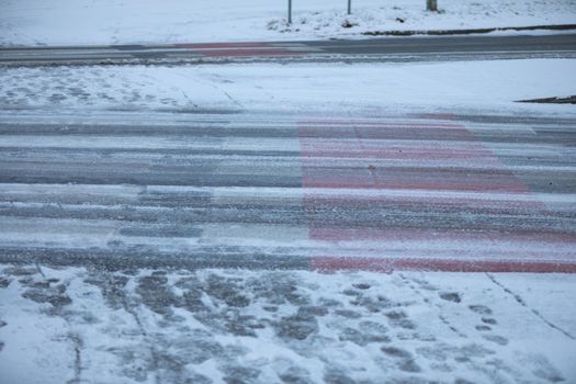 Uncleared street and pedestrian crossing of snow and frozen ice. More dangerously slippery at the pedestrian crossing.