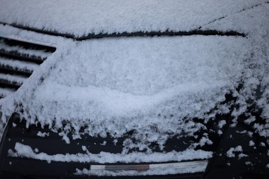 The body of the car covered with a thin layer of white snow. Winter weather is not favourable for drivers.