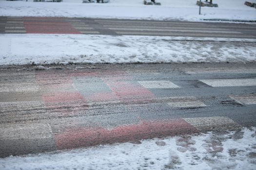 Uncleared street and pedestrian crossing of snow and frozen ice. More dangerously slippery at the pedestrian crossing.