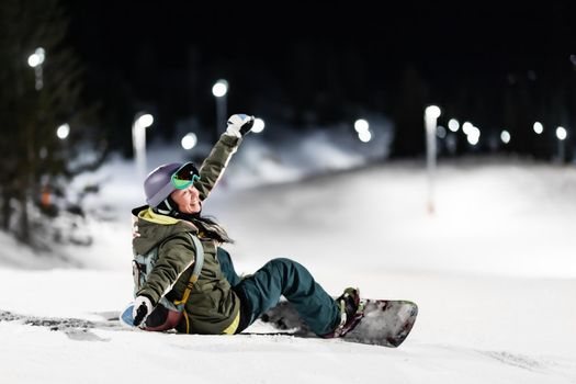 Snowboarder girl posing on slopes. Night skiing in winter resort.