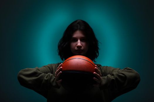 Teenage girl with basketball. Studio portrait with neon blue colored background.