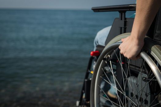 Caucasian woman in a wheelchair on the seashore. Close-up of female hands
