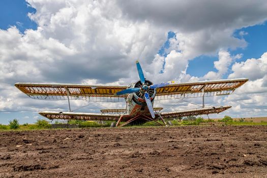 Abandoned aircraft plane standing in the field against the cloudy blue sky. 