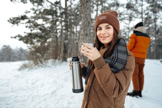 Young woman with hot drink thermos at winter forest, close up