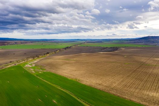 Amazing wide aerial view from drone of beautiful green countryside, fields, road, and cloudy sky