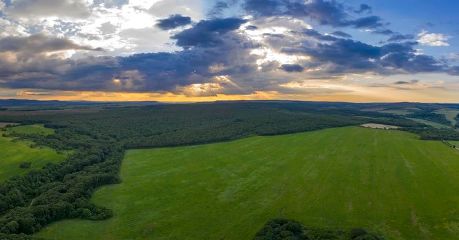 Amazing panoramic view of cloudy sky with sun rays over green field and forest