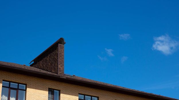 A roof with a chimney on the background of a blue summer sky.