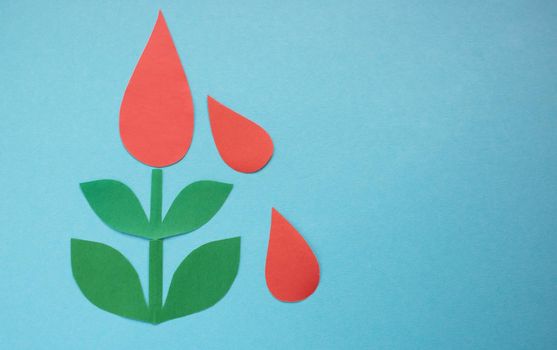 Drops of blood from paper on a green tree on a blue background.The concept of the World Blood Donor and Hemophilia Day.