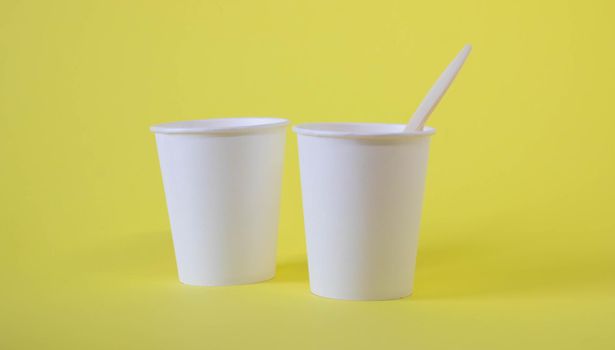 Two small white paper cups on a yellow background.