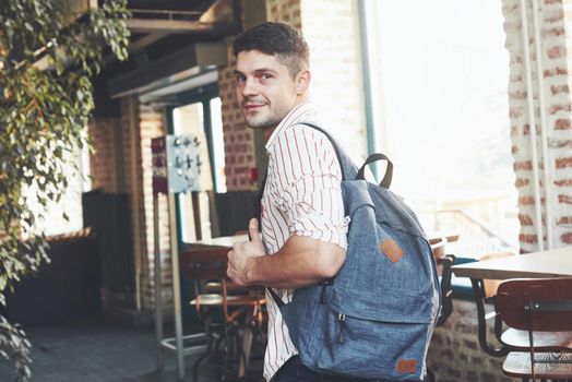 Looking behind. Man in casual clothes and backpack stands indoors.