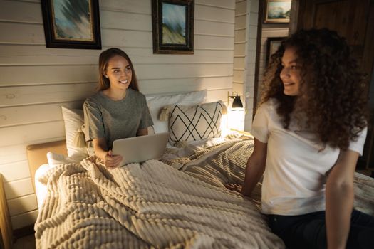Two beautiful women lying in bed, holding and watching laptop
