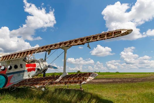 Abandoned aircraft plane standing in the field against the cloudy blue sky. 