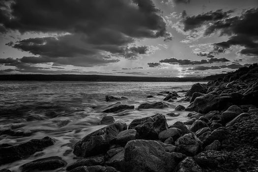 Stunning sunset over the sea with the rocky sea coast in black and white.