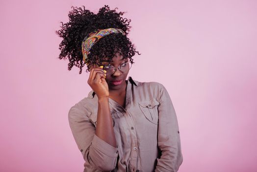 Trying on new glasses. Attractive afro american woman in casual clothes at pink background in the studio.