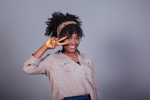 Showing gesture of two fingers near the eyes. Attractive afro american woman in casual clothes in the studio.