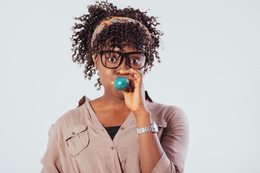 Inflates a blue ball. Beautiful afro american girl with curly hair in the studio with white background.
