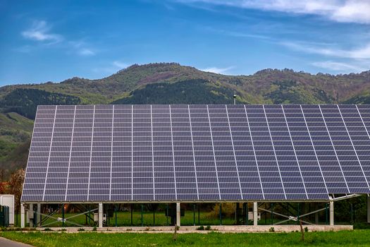 Many solar panels at the field. Horizontal orientation, blue sky, gray panels , mountain at background