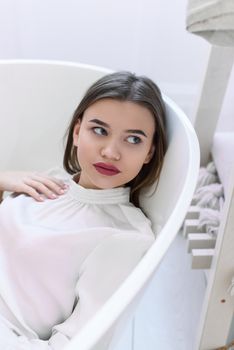 Portrait of fashionable women in a white blouse posing in a bath. Girl with a big red lips